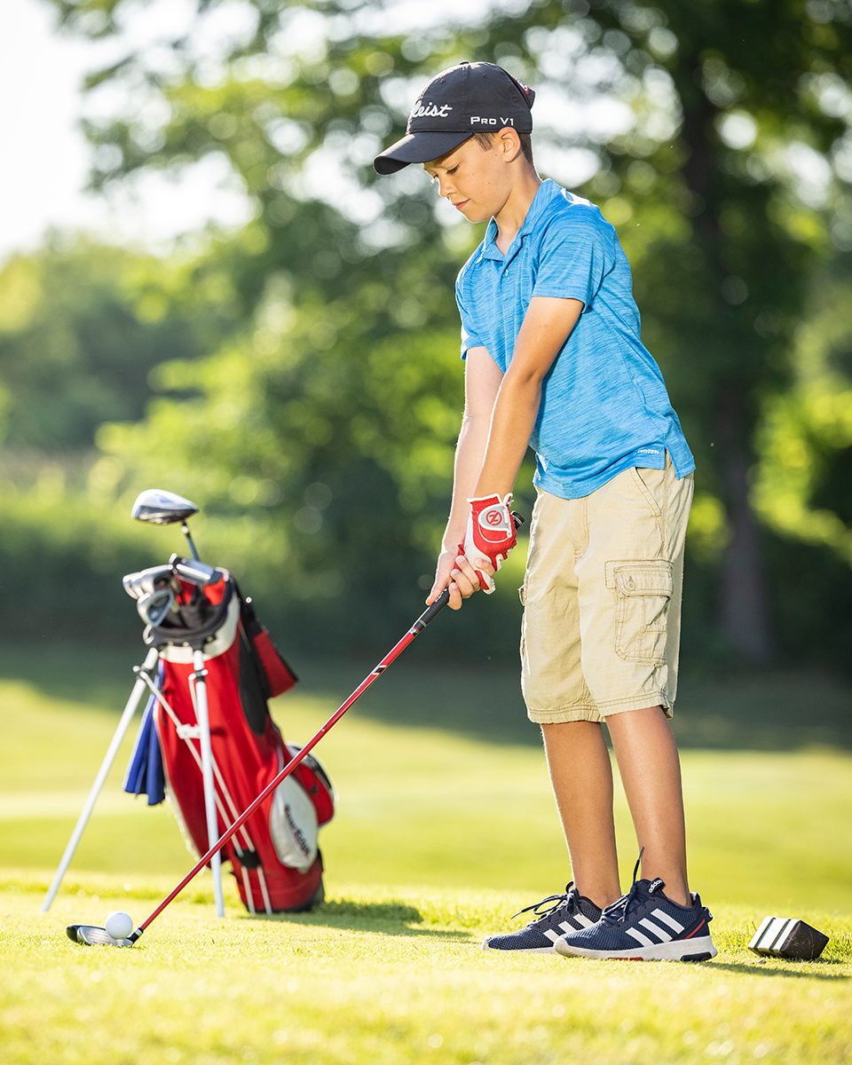 boy with a golf bag in front lining up a tee shot